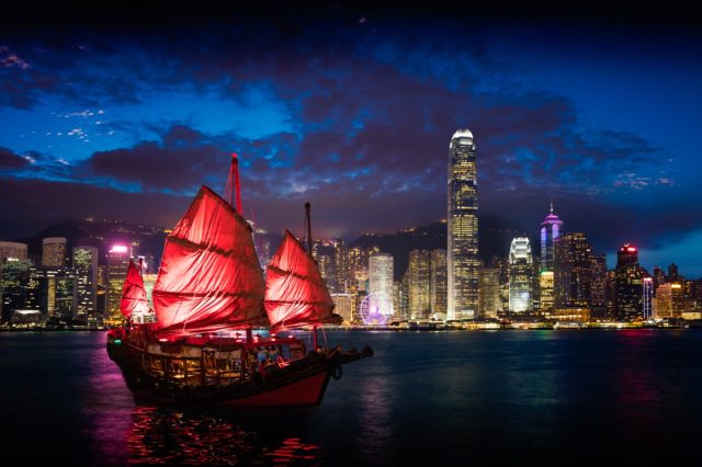 Victoria Harbour, Hong Kong night view with junk ship on foreground.