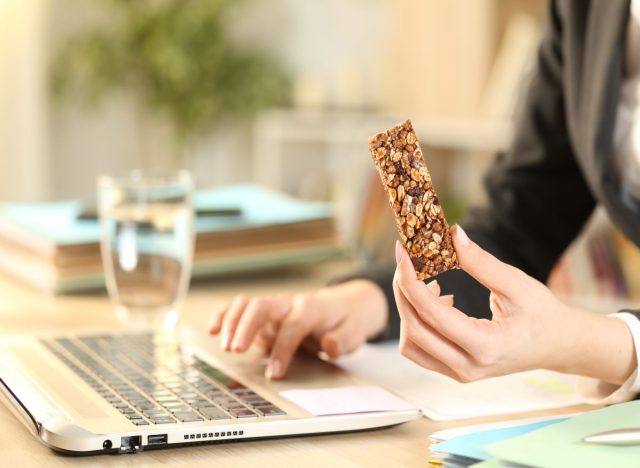 Woman eating muesli bae with laptop