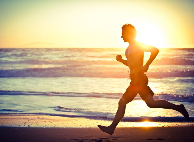 man barefoot running on beach at sunset