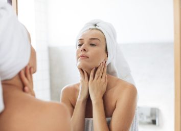 woman touching her neck, skincare, looking in bathroom mirror