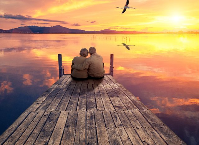 older couple sitting on dock on lake at sunset