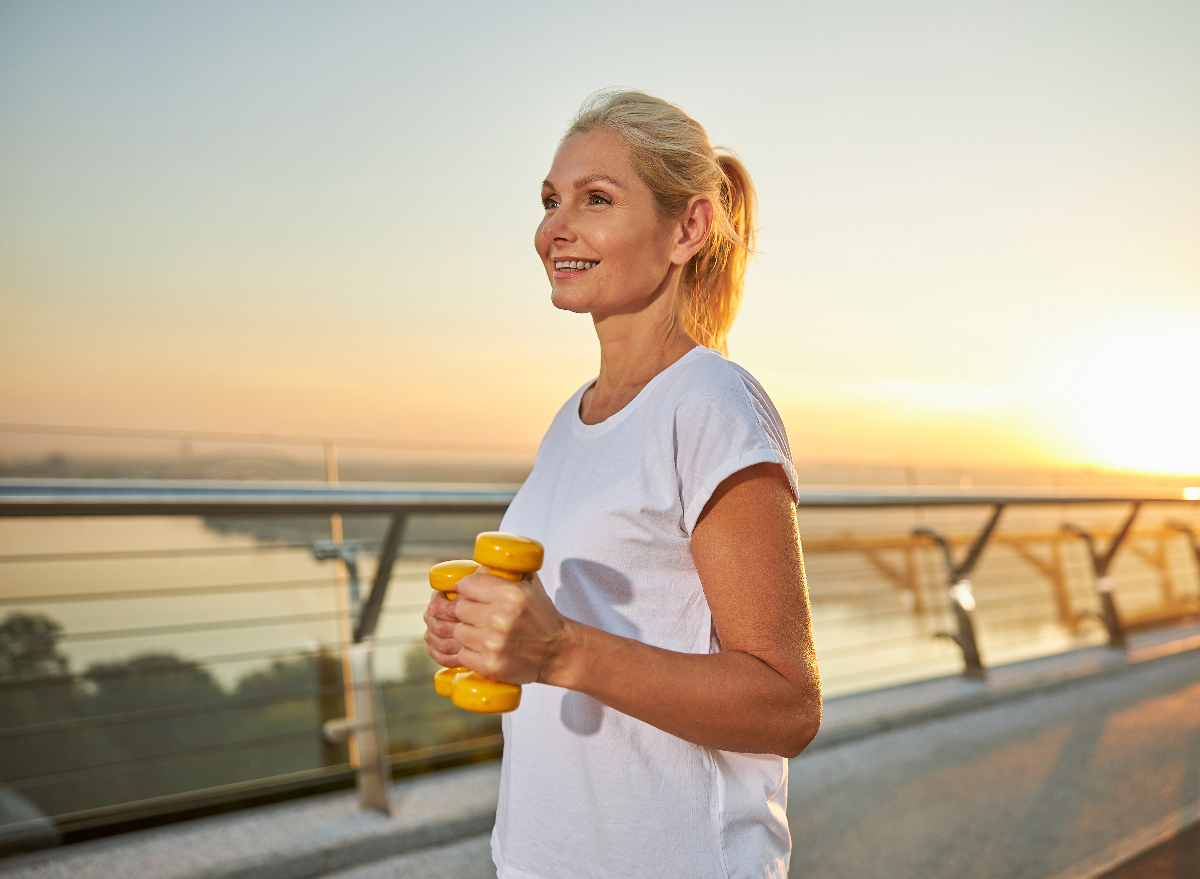 happy woman does walking workout at sunset with dumbbells