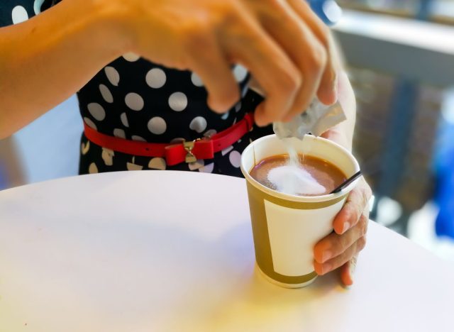 Woman pouring sugar into coffee