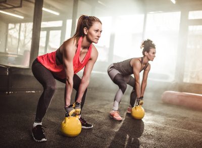 two women performing kettlebell deadlifts to lose belly fat for good