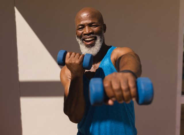Bărbat fericit în vârstă de cincizeci de ani ținând gantere pentru antrenamentul HIIT pentru a accelera procesul de pierdere a grăsimii de pe burtă