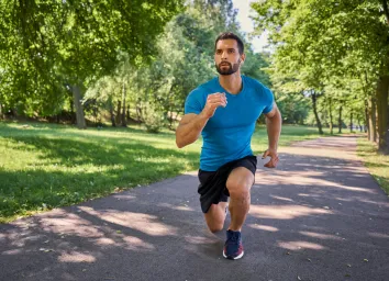 man going lunges to tone sagging leg skin while walking outdoors on paved trail, sunny day