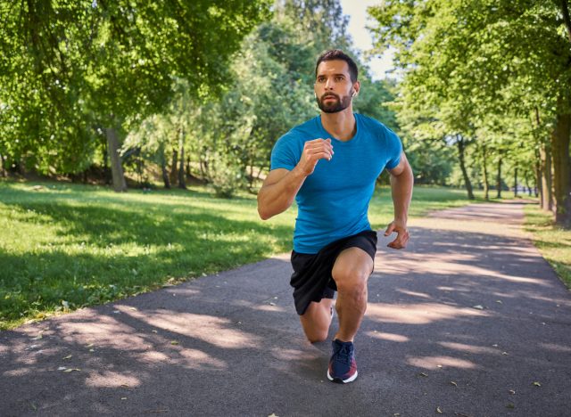 man going lunges to tone sagging leg skin while walking outdoors on paved trail, sunny day