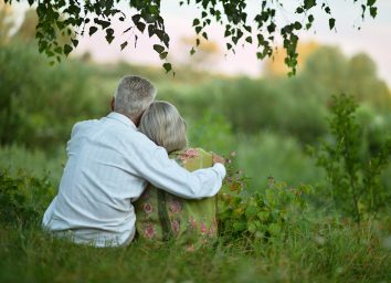 old senior couple snuggling outside looking out into lush park