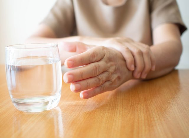 closeup older woman with Parkinson's disease reaching for water glass