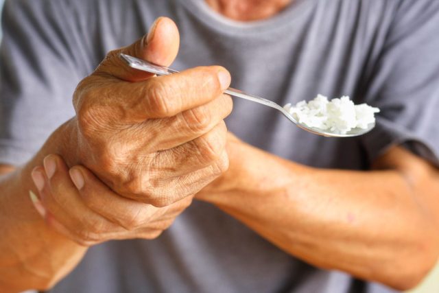 closeup older individual with parkinson's holding spoon with rice