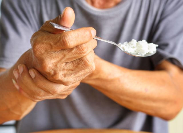 closeup older individual with Parkinson's disease holding spoon with rice