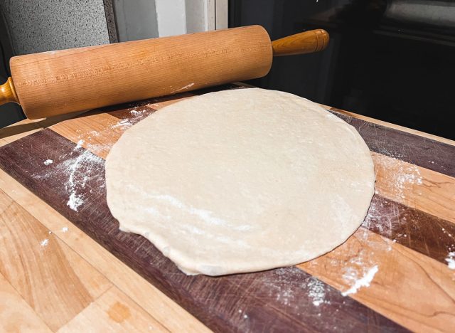 rolling out pizza dough on a cutting board