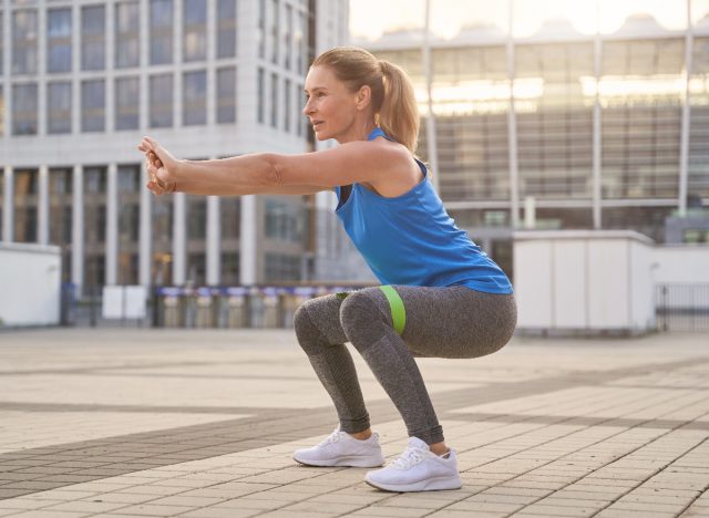 Une femme d'âge moyen en forme démontre des exercices de squat avec une bande de résistance pour soulever ses fesses