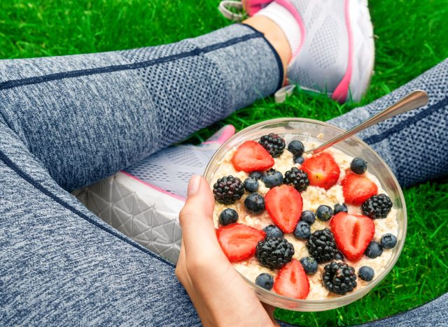 female runner sits on grass while eating berries with oatmeal