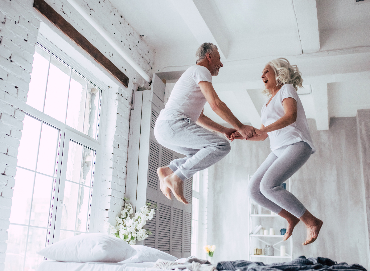 seniors having fun jumping up on bed in bright bedroom