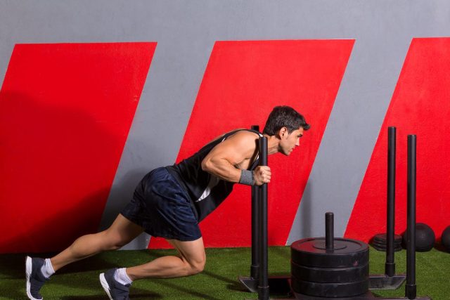 man doing sled push at gym to speed up belly fat loss