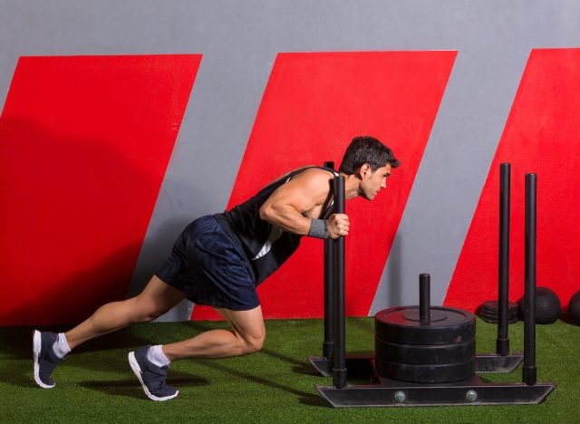 man doing sled push at gym to speed up belly fat loss