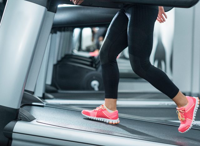 mujer de primer plano caminando en la cinta de correr inclinada para acelerar la pérdida de grasa abdominal en el gimnasio durante el entrenamiento de la cinta de correr