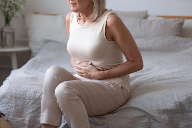 mature woman dealing with bad gut health, stomach pain on bed