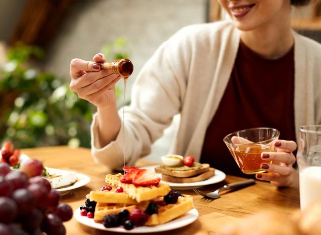 woman adding honey to a plate of healthy protein waffles