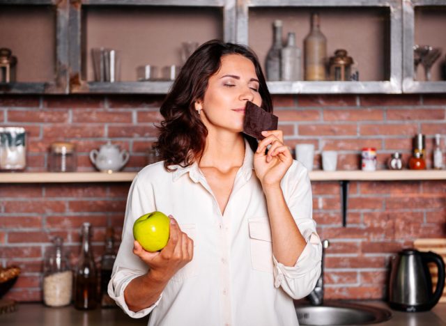 woman holding apple and chocolate, having cravings