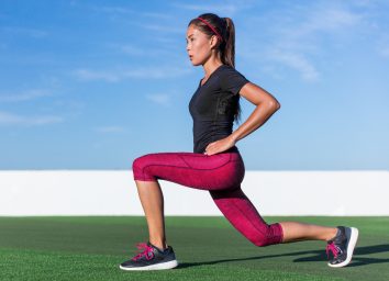 woman performing jumping lunge during cardio workout outdoors to shrink belly fat