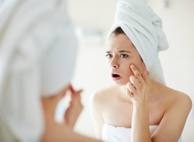 surprised woman looking in bathroom mirror at acne on cheek