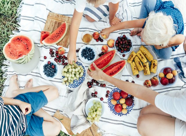 People eating fruit on a picnic blanket