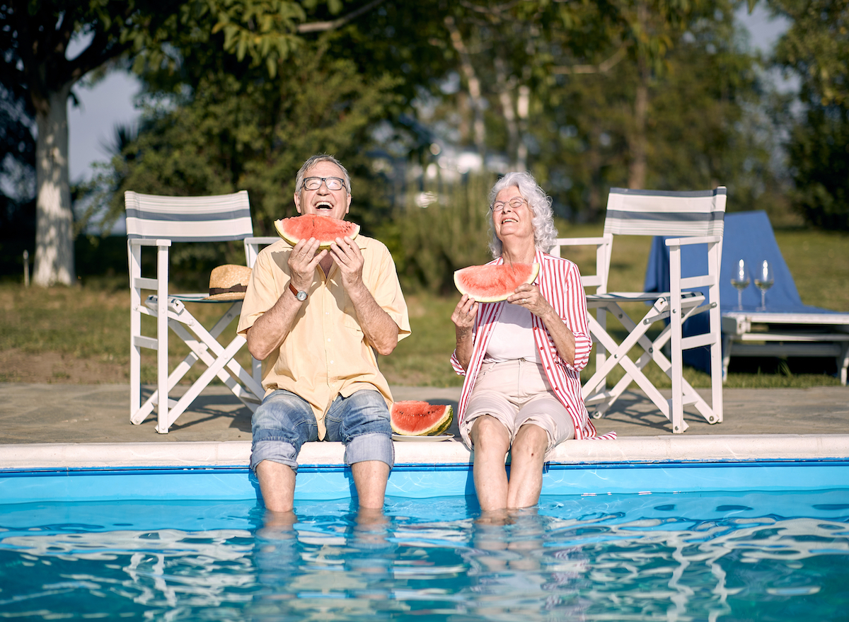 Old couple eating watermelon by the pool