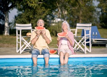 Old couple eating watermelon by the pool