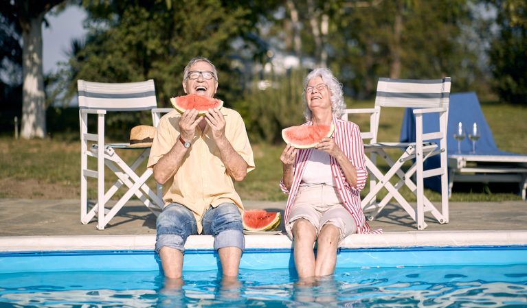 Old couple eating watermelon by the pool
