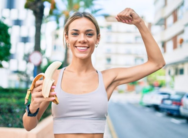 woman flexing while eating banana outside