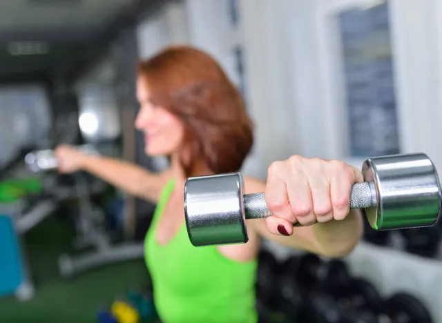 Mujer madura haciendo entrenamiento de modelado del cuerpo de elevación lateral con mancuernas