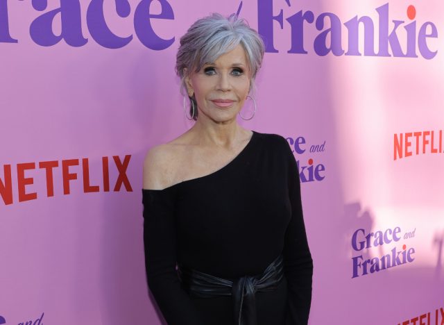 Jane Fonda in black jumpsuit posing in front of hot pink backdrop