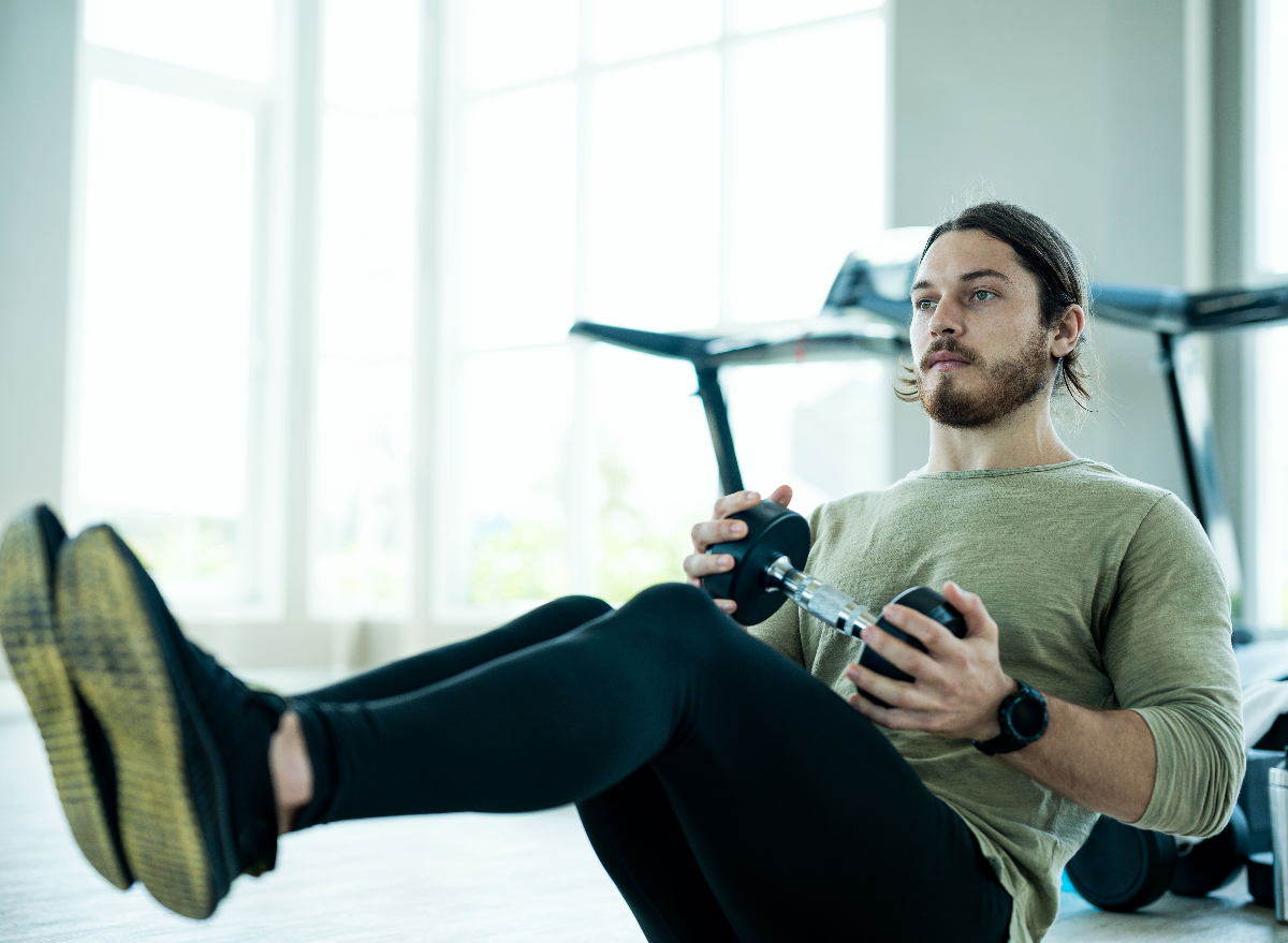 man performing dumbbell crunches in bright gym to get rid of belly creases