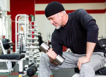 mature man lifting weights in gym, slimming down after 60
