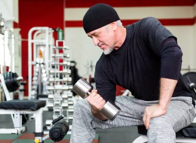 mature man lifting weights in gym, slimming down after 60