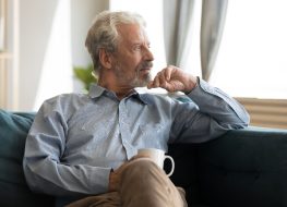 older man sitting at home with coffee, looking out window, Alzheimer's