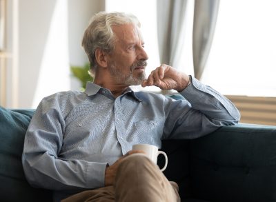 older man sitting at home with coffee, looking out window, Alzheimer's