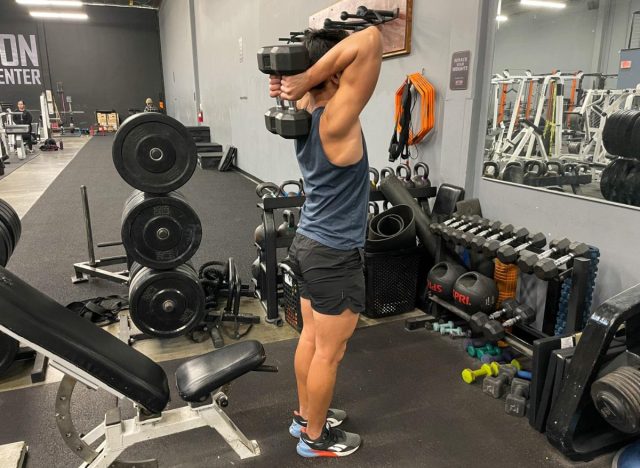 trainer demonstrating overhead dumbbell triceps extension