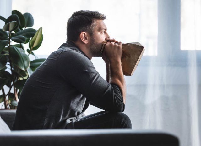 man experiencing panic attack, breathing into paper bag