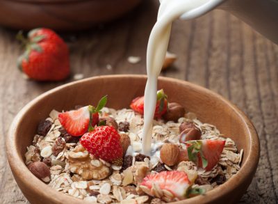 pouring milk into bowl of oats, fruit, and nuts