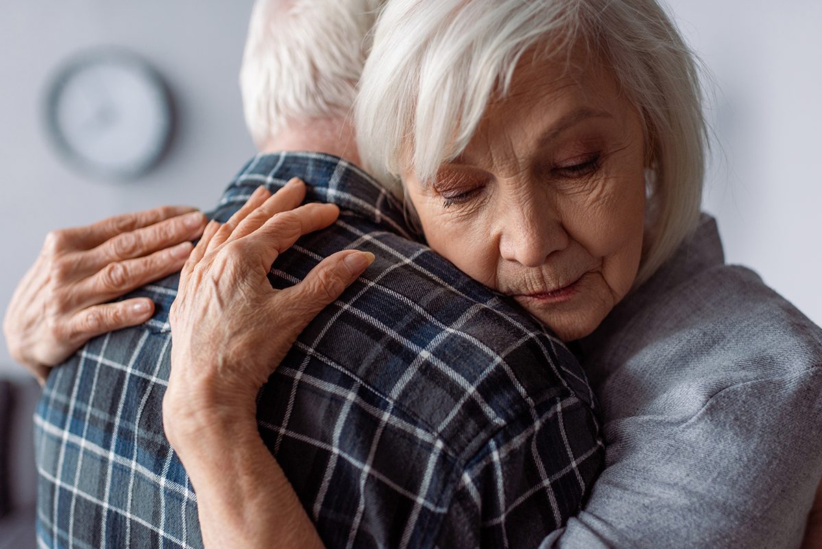 Senior,Woman,With,Closed,Eyes,Embracing,Husband,Sick,On,Dementia