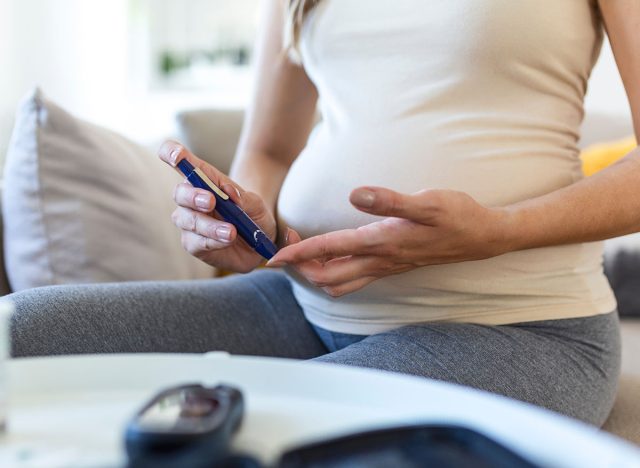 Blood sugar testing at home.  Pregnant Woman Checking Blood Sugar Level At Home.  Diabetic Checking Blood Sugar Levels.  Pregnant Woman checking blood sugar level by glucometer and test stripe at home
