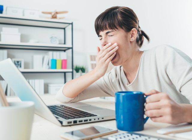 sleepy woman wondering why am I always tired yawns at desk while doing work
