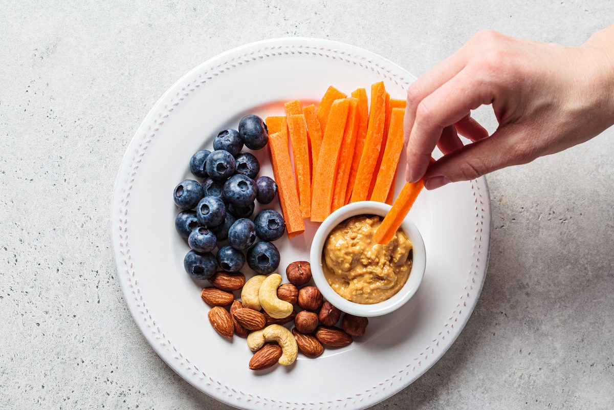 snack plate with carrots, peanut butter, nuts, and blueberries