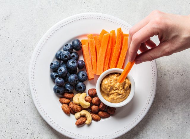snack plate with carrots, peanut butter, nuts, and blueberries