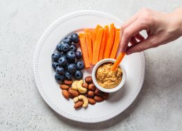 snack plate with carrots, peanut butter, nuts, and blueberries