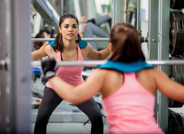 Woman breaking plateau doing barbell squat in gym