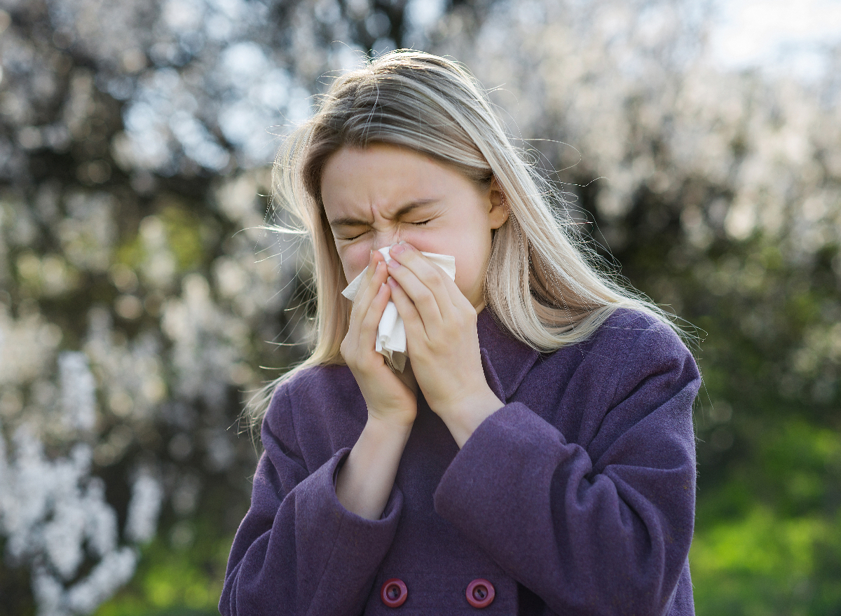 blonde woman blowing nose outside, dealing with side effects of seasonal allergies